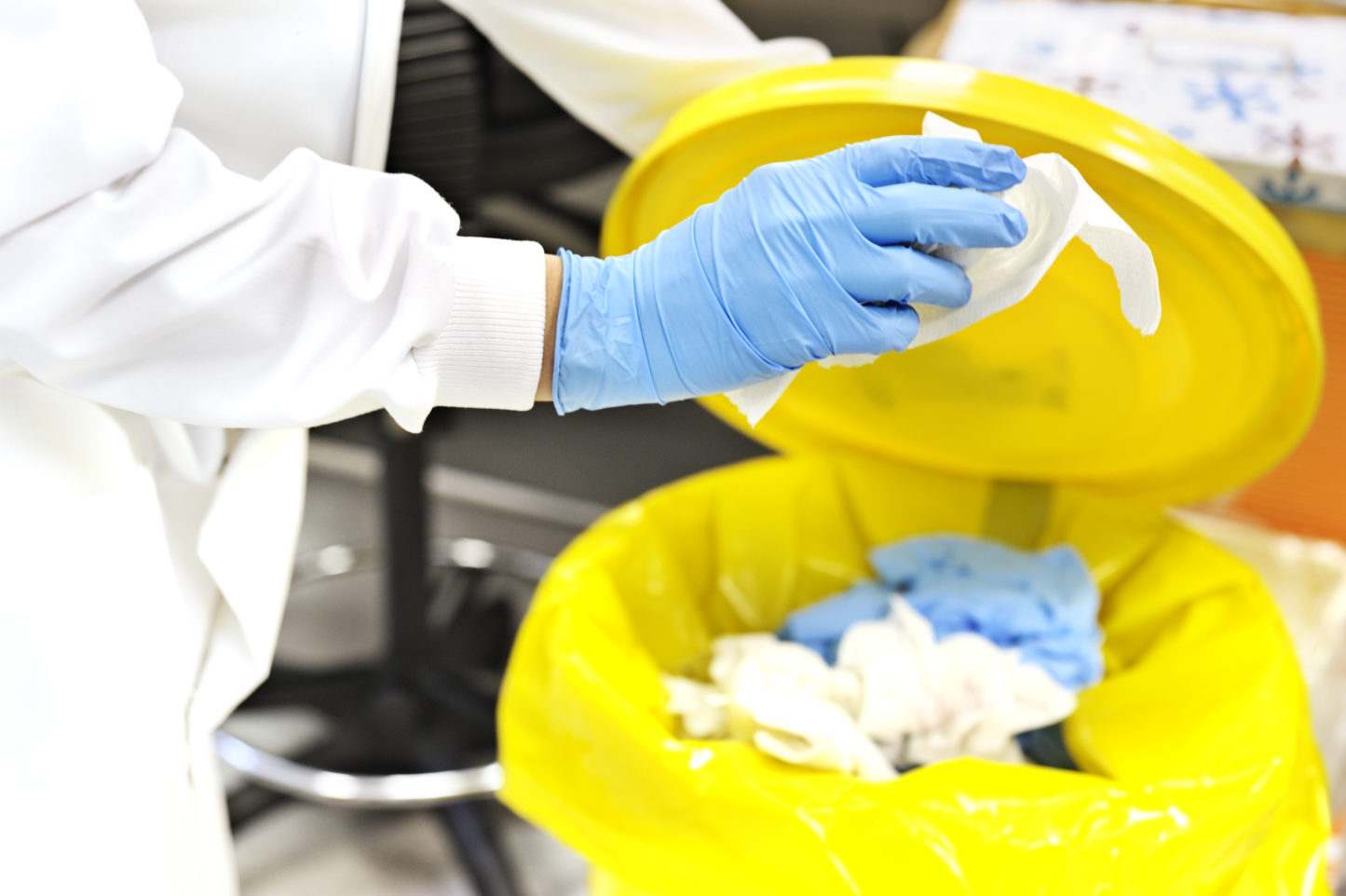 Lab worker putting biohazard items in regulated medical waste containers.